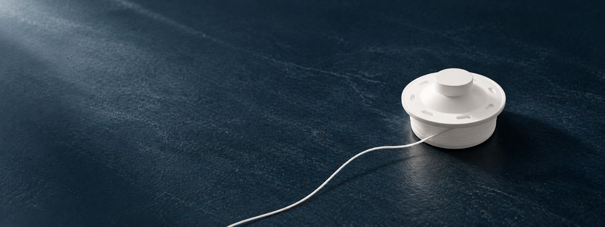 White Flossy refill spool with a curved strand of floss on a dark blue stone surface